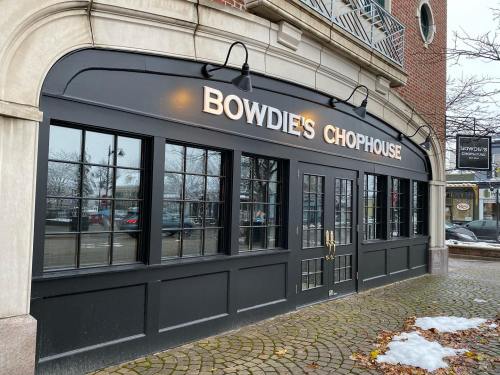 Exterior of Bowdie's Chophouse featuring large windows and a black facade, with a brick building in the background.