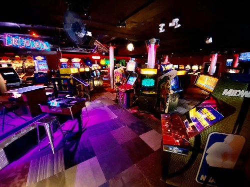 A vibrant arcade filled with classic video game machines and skeeball, illuminated by colorful lights.