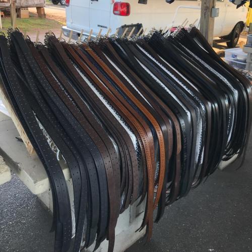 A variety of leather belts in different colors and styles hanging on a display rack.