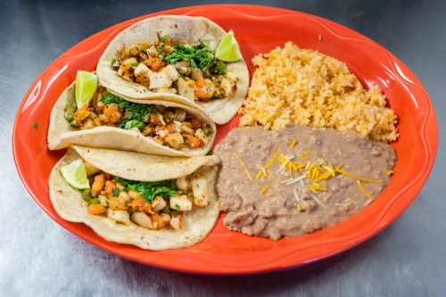A vibrant plate featuring three tacos with toppings, rice, and refried beans, garnished with lime wedges.
