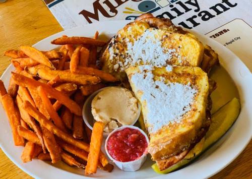 A plate of French toast dusted with powdered sugar, served with sweet potato fries and dipping sauces.