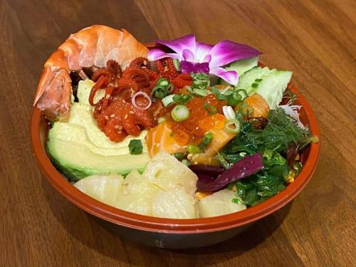 A colorful seafood bowl with shrimp, octopus, avocado, seaweed, and garnished with flowers and green onions.