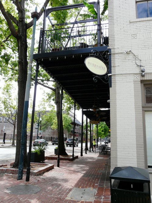 A street view of a restaurant with outdoor seating, surrounded by trees and brick pavement.