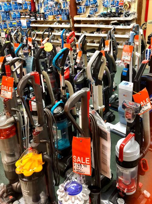 A variety of vacuum cleaners on display in a store, many with sale tags and colorful designs.
