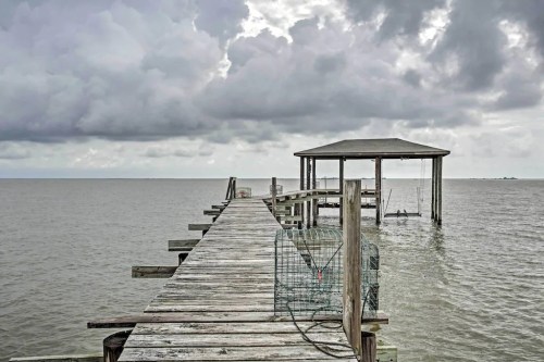 A weathered wooden pier extends into a calm sea under a cloudy sky, with a small gazebo at the end.