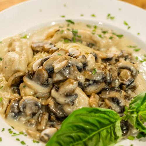 A plate of creamy pasta topped with sautéed mushrooms and fresh basil, garnished with chopped herbs.