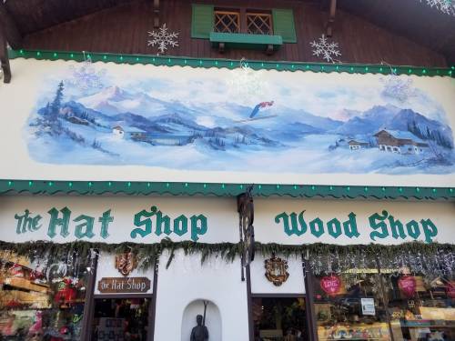 A charming shop facade featuring a mural of mountains and snow, with signs for "The Hat Shop" and "Wood Shop."