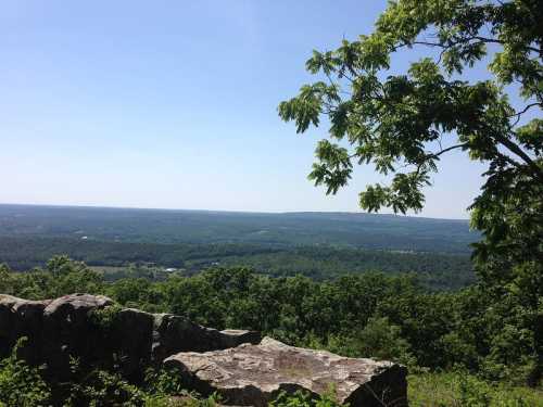 A scenic view from a rocky overlook, showcasing lush green hills and a clear blue sky.