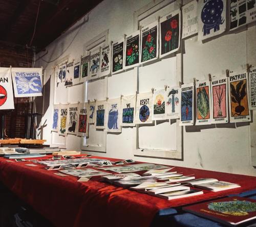 A display of art prints and books on a table, with colorful posters hanging on the wall behind.
