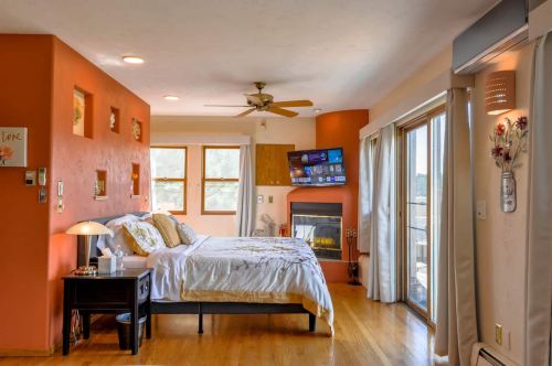 Cozy bedroom with two beds, a fireplace, large windows, and a TV mounted on the wall. Warm orange walls enhance the ambiance.