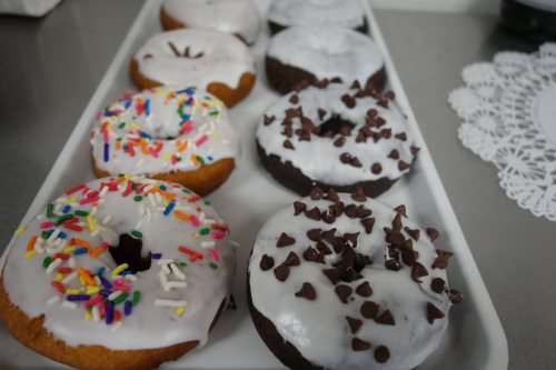 A tray of assorted donuts with white icing, colorful sprinkles, and chocolate chips.