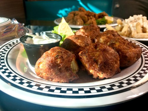 A plate of golden-brown fritters served with a lime wedge and a small cup of dipping sauce.