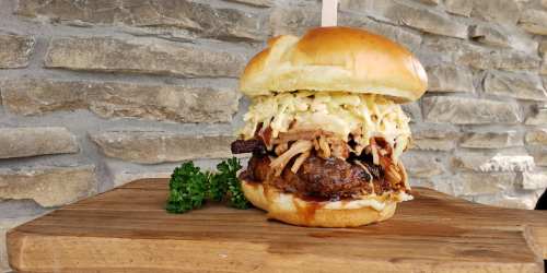 A delicious burger stacked with pulled pork and coleslaw, served on a soft bun with a garnish of parsley.