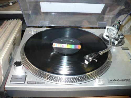A close-up of a turntable with a vinyl record spinning, showcasing the stylus and colorful label on the record.
