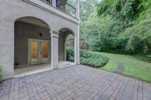 Patio area with arched entry, stone pavers, and lush greenery in the background.