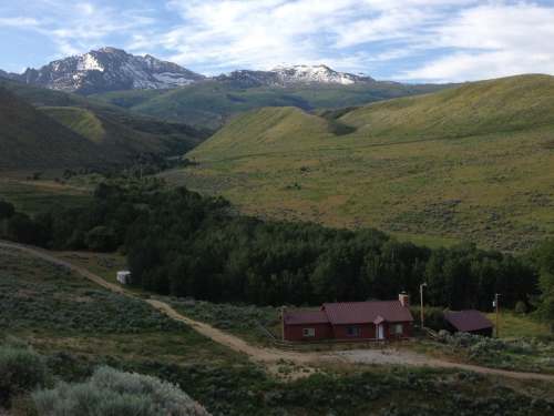 A scenic view of a valley with rolling green hills, a small house, and snow-capped mountains in the background.