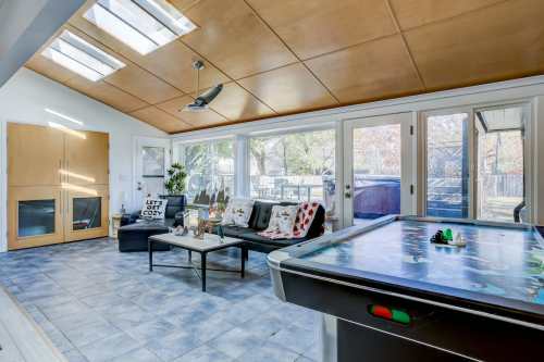 Bright, modern living space with large windows, a pool table, and stylish furniture, featuring a wooden ceiling.