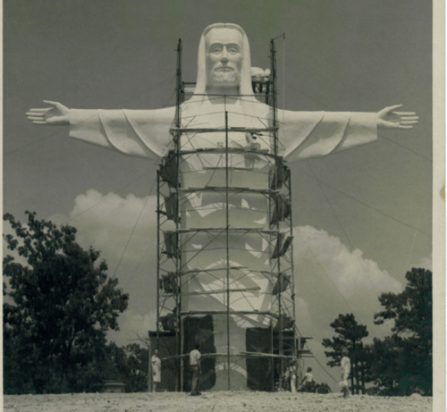 Historic photo of a large statue of Christ being constructed, surrounded by scaffolding and workers.