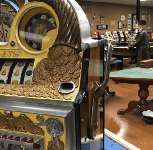 Close-up of a vintage slot machine with coins, set in a retro gaming room with other machines in the background.