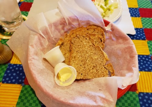A basket of brown bread slices with a small cup of butter on a colorful tablecloth.