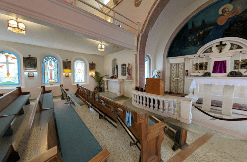 Interior of a church featuring wooden pews, stained glass windows, and an altar with religious decorations.