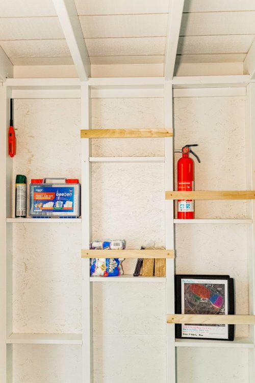 A white shelving unit with tools, a fire extinguisher, and various supplies neatly organized on the shelves.
