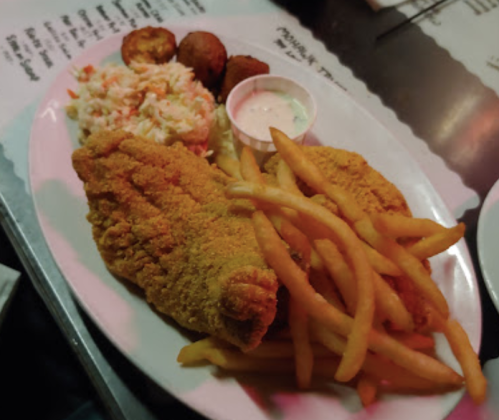 A plate of fried fish fillets, French fries, coleslaw, and hushpuppies with a small cup of dipping sauce.