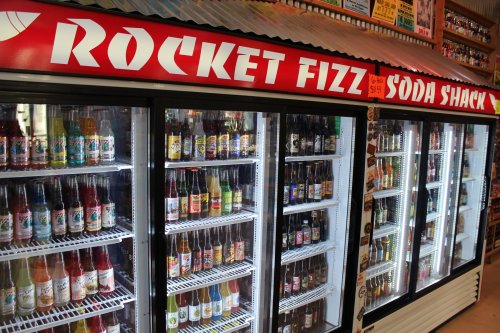 A colorful display of various soda bottles in a refrigerated section at Rocket Fizz Soda Shack.