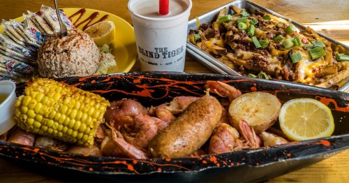 A vibrant seafood platter with shrimp, sausage, corn, and lemon, alongside loaded nachos and a drink.