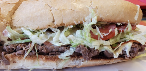 A large sandwich filled with sliced beef, lettuce, tomatoes, and mayonnaise on a crusty bread roll.