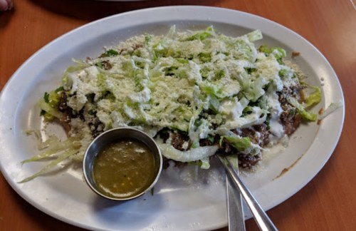 A plate of food topped with shredded lettuce, cheese, and a side of green salsa.