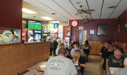 A busy diner with patrons eating, a TV showing a game, and a counter with staff serving food.