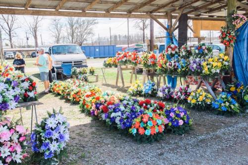 A vibrant flower market with colorful artificial flowers displayed on tables under a shelter.