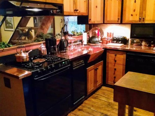Cozy kitchen with wooden cabinets, a black stove, and a copper countertop, featuring various kitchen appliances and decor.