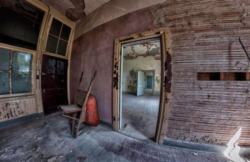Abandoned interior with peeling walls, a chair, and doorways leading to empty, dilapidated rooms.