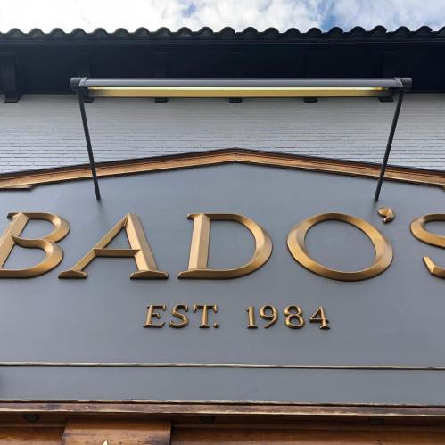 Sign for Bado's, established in 1984, featuring gold lettering on a gray background.