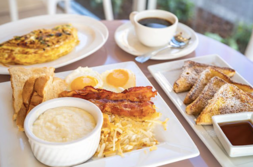 A breakfast spread featuring an omelette, eggs, bacon, hash browns, toast, French toast, and a cup of coffee.
