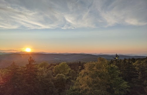 Sunset over a mountainous landscape, with trees in the foreground and a colorful sky.