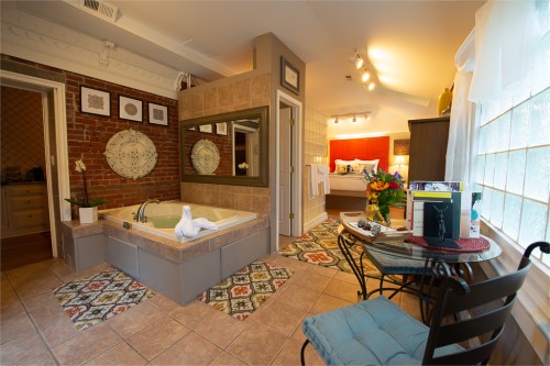 A cozy bathroom featuring a jetted tub, decorative tiles, and a small seating area with flowers and a laptop.
