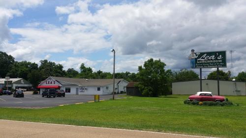 A roadside view of Lea's Lunchroom, featuring a sign, parking lot, and a classic car in front of a green landscape.
