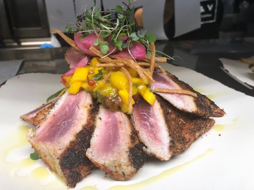 A beautifully plated dish featuring seared tuna slices, mango salsa, pickled onions, and crispy garnishes.