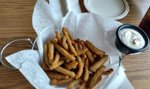 A basket of crispy fried green beans served with a small cup of dipping sauce on a wooden table.