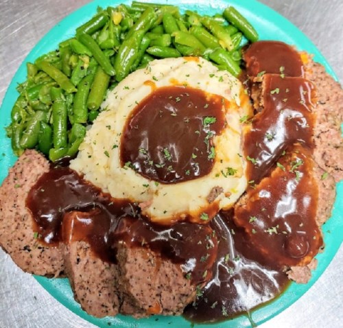 A plate of meatloaf with brown gravy, mashed potatoes, and green beans, garnished with parsley.