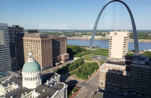 View of the St. Louis Arch with city buildings and the Mississippi River in the background on a clear day.