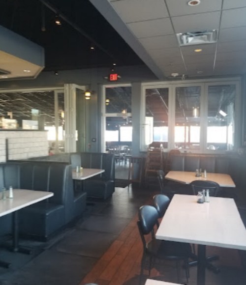 Interior of a restaurant featuring empty booths and tables, with large windows and modern decor.