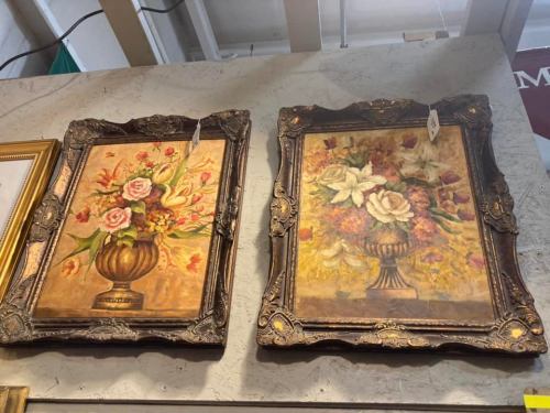 Two vintage floral paintings in ornate frames, featuring vases of roses and lilies, displayed on a wall.