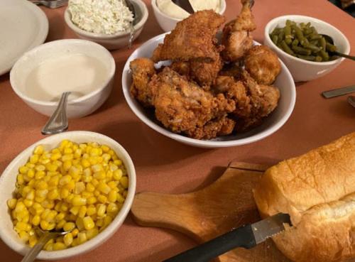 A table spread with fried chicken, corn, coleslaw, green beans, creamy sauce, and sliced bread.