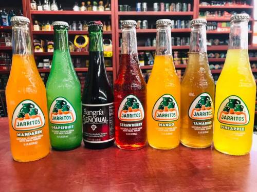 A variety of colorful beverages, including Jarritos sodas in mandarin, grapefruit, mango, tamarind, and pineapple, plus a bottle of sangría.