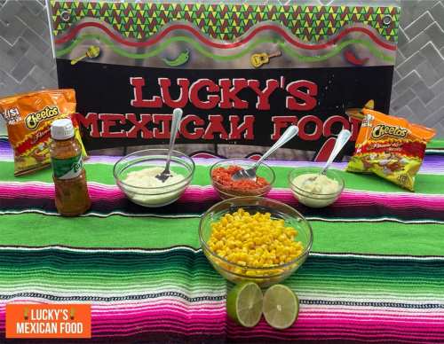 A colorful spread of Mexican food with bowls of sauces, corn, and snacks on a vibrant tablecloth.