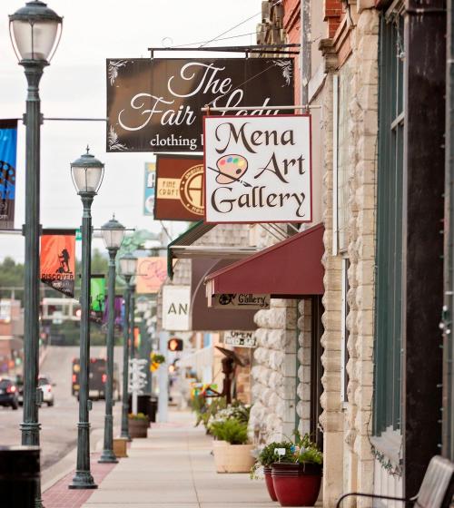A street view featuring storefronts, including The Fair Lady clothing store and Mena Art Gallery, with decorative street lamps.